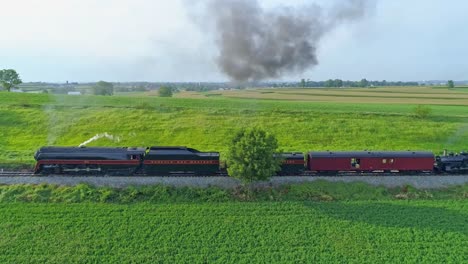 Una-Vista-Aérea-De-Un-Tren-De-Vapor-No-611-Que-Sopla-Humo-A-Través-Del-Campo-Agrícola-En-Un-Día-Soleado-De-Verano-Con-Campos-Verdes