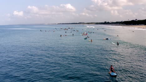 Large-group-of-surfers-waiting-for-waves-on-a-sunny-day-at-a-famous-surfing-spot,-Aerial-drone-flyout-reveal-shot