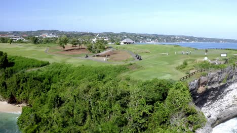 Nuevo-Campo-De-Golf-De-Kuta-Con-Jugadores-Cerca-Del-Acantilado-Oceánico-Y-Una-Gran-Estatua-De-Golfista-En-La-Playa-De-Balangan,-órbita-Aérea-Alrededor-Del-Tiro