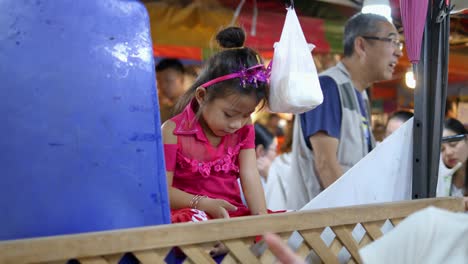 Young-girl-sitting-playing-bored-on-her-phone-busy-night-market,-Bangkok