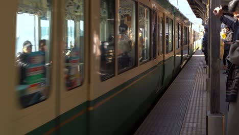 Enoden-Train-driving-into-Kamakurakoukoumae-station-with-backdrop-of-Enoshima,-Kamakura,-Japan