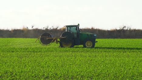 Tractor-places-plastic-drips-in-a-corn-field,-Green-corn-field,-At-sunset,-John-Deere-Tractor,-Slow-Motion