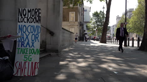 Ein-Mann-In-Einem-Anzug-In-Whitehall-In-Westminster-Geht-An-Einem-Protestplakat-Gegen-Die-Coronavirus-Verschwörungstheorie-Vorbei,-Auf-Dem-Steht:-„Keine-Sperrung-Mehr