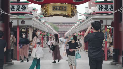 Japoneses-Con-Máscara-Facial-Mientras-Toman-Fotos-De-La-Famosa-Puerta-Kaminarimon-Durante-El-Brote-De-Coronavirus-En-Asakusa,-Tokio,-Japón---Tiro-Medio-Completo