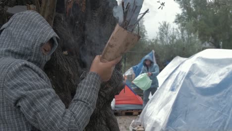 Joven-En-El-Campo-De-Refugiados-De-Moria-Encendiendo-Cartón-Húmedo-Para-Hacer-Fuego-En-Las-Duras-Condiciones-Invernales