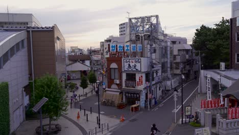 Typical-residential-area-in-Japanese-city-with-storefronts-and-people-driving-on-bicycles-at-sunset