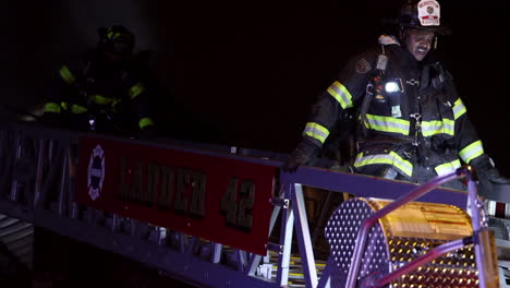 Un-Bombero-Desciende-Una-Escalera-En-Plena-Marcha-Después-De-Combatir-El-Incendio-De-Una-Casa-Por-La-Noche