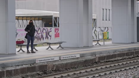 Einsame-Frau-Mit-Maske,-Die-Auf-Dem-Bahnsteig-An-Einem-Bahnhof-In-Arcore,-Norditalien,-Wartet