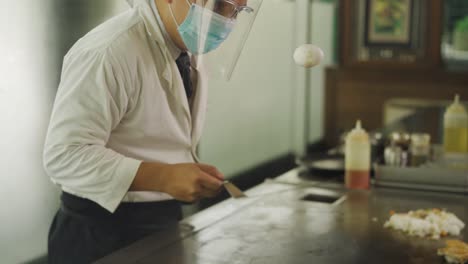 Chef-Wearing-Mask-And-Face-Shield-Does-A-Juggling-Act-With-An-Egg-And-A-Spatula