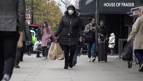 Una-Toma-En-Cámara-Lenta-De-Personas-Con-Bolsas-De-Compras-Caminando-Por-Oxford-Street-Mientras-Se-Implementa-El-Nuevo-Sistema-De-Tres-Niveles-De-Regulación-Covid,-Que-Permite-Que-Negocios-No-Esenciales-Abran-Antes-De-Navidad