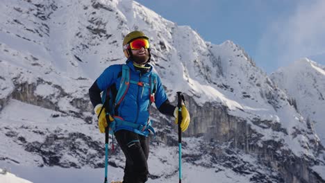 Bearded-skier-with-snow-goggles-smiles-in-front-of-snow-mountain