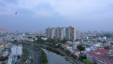 Volar-En-Tomas-De-Drones-De-Edificios,-Puesta-De-Sol,-Puente,-Canal,-Reflexión-Y-Expansión-Urbana-Del-Distrito-Ocho-De-La-Ciudad-De-Ho-Chi-Minh