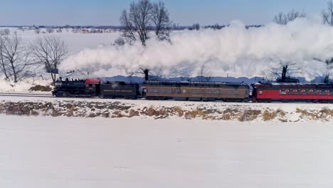 Luftaufnahme-Einer-Antiken-Dampflokomotive,-Die-Sich-Nähert,-Um-Personenwagen-Zu-Ziehen-Und-Rauch-Und-Dampf-Nach-Einem-Schneesturm-Zu-Blasen