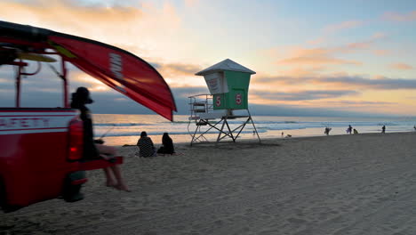 Leute,-Die-Auf-Dem-Sand-Am-Strand-Sitzen,-Mit-Einem-Rettungsschwimmerfahrzeug,-Das-Im-Vordergrund-Vorbeifährt