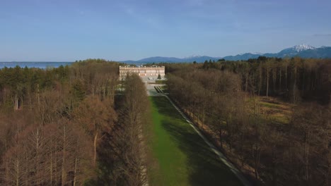 Vista-Aérea-Escénica-De-4k-Sobre-La-Famosa-Isla-Del-Castillo-Herrenchiemsee-De-Baviera-Y-Su-Parque-Real-En-El-Lago-Chiemsee-En-El-Campo-Rural-Con-Un-Hermoso-Cielo-Azul-Y-Las-Montañas-De-Los-Alpes-En-El-Fondo