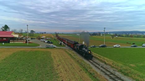 Una-Vista-Aérea-De-Un-Antiguo-Tren-De-Vapor-Restaurado-Y-Vagones-De-Pasajeros-Que-Se-Acercan-Con-Humo-Y-Vapor-Con-Turistas-Y-Espectadores-Mirando-Como-Los-Ve-Un-Dron