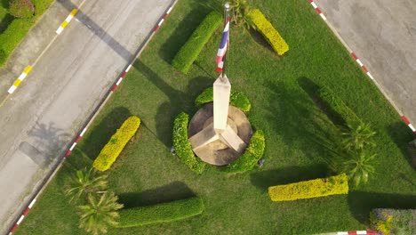 Thailändische-Nationalflagge-Auf-Einer-Stange-Mit-Sockel,-Eine-Absteigende-Luftaufnahme-Der-Thailändischen-Flagge,-Die-Den-Sockel-Und-Das-Gras-Enthüllt