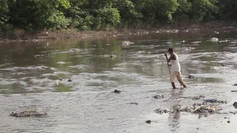 Un-Niño-Cruza-Un-Río-En-Pakistán,-Tirado-Con-Basura-Tóxica-En-El-Agua