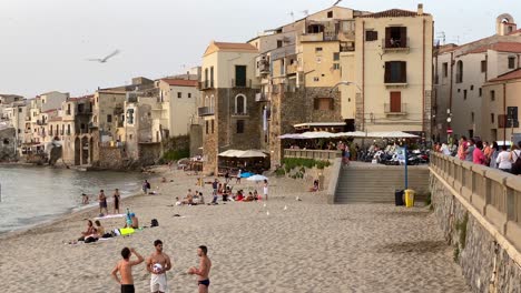 Puesta-De-Sol-En-Una-Playa-Y-Paisaje-Urbano-Con-Gaviotas-Y-Gente-Descansando-Y-Hablando