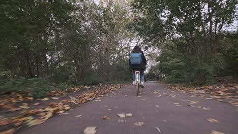 Tiro-De-Seguimiento-Bajo-De-Una-Mujer-Joven-En-Bicicleta-A-Lo-Largo-De-Un-Camino-Tranquilo-Otoño