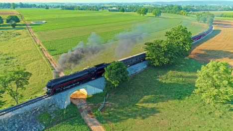 Luftaufnahme-Einer-Antiken-Dampfmaschine-Und-Personenwagen,-Die-An-Einem-Sonnigen-Sommertag-Entlang-Der-Landschaft-Fahren-Und-Rauch-Und-Drohnen-Vor-Sich-Herziehen