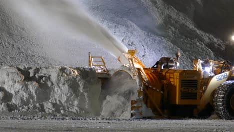 Soplador-De-Nieve-Montado-En-El-Cargador-En-Funcionamiento-Para-Soplar-Nieve-Encima-De-La-Nieve-Mientras-Un-Tractor-Pasa-Por-La-Noche