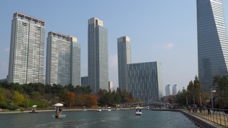 Posco-Tower-Y-Songdo-Central-Park-En-Incheon-Con-Personas-Que-Viajan-En-Botes-Y-Caminan-Por-El-Lago-Con-Máscaras-Faciales-Durante-Covid-19-Con-Rascacielos-De-Gran-Altura-Contra-El-Cielo-Despejado