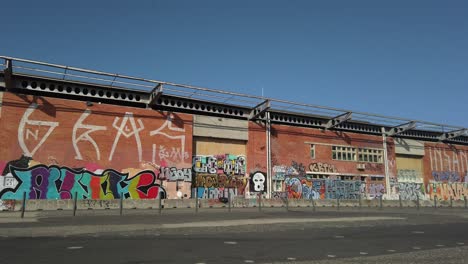 Atleta-Masculino-Cuerpo-Musculoso-Haciendo-Ejercicios-En-La-Calle-Al-Lado-Del-Edificio-Del-Almacén-De-Pared-De-Graffiti-Y-Ciclista-Pasando-En-Lisboa