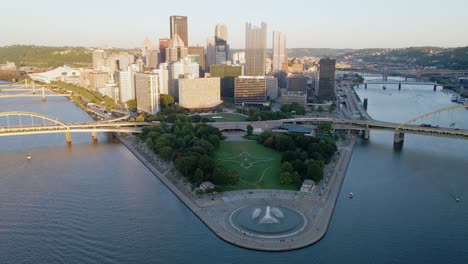 Luftaufnahme-Des-Springbrunnens-Im-Point-State-Park-Und-Der-Sonnenbeschienenen-Skyline-Von-Pittsburgh---Neigung,-Drohnenaufnahme