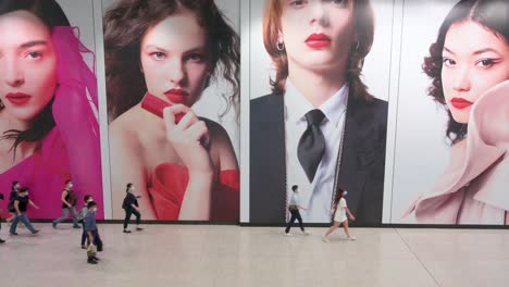 People-commute-to-go-to-work-as-they-walk-past-a-large-commercial-advertisement-banner-at-Hong-Kong-MTR-subway-station-early-morning-in-Central-district,-Hong-Kong