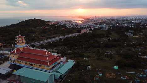 Buddhist-shrine-and-panorama-of-Phan-Thiet-city,-Vietnam,-aerial-view-at-sunset