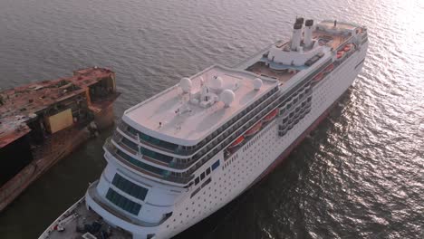 Aerial-Over-Large-White-Cruise-Ship-Beached-Next-To-Rusty-Hull-At-Gadani