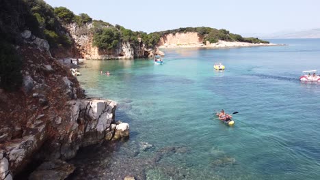 Tourist-Couple-Kayaks-to-Ksamil-Islands,-Albania---Aerial-Dolly-Follow