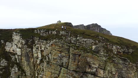 Two-Hikers-on-Cliff-Edge-of-Horn-Head,-Ireland---Aerial-Pullaway