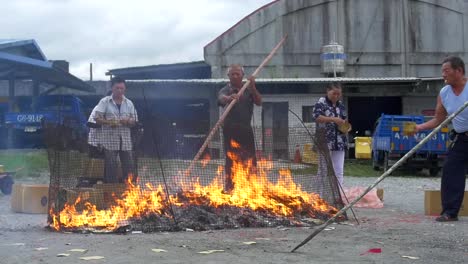 Asian-man-using-large-bamboo-stick-to-stir-burning-paper-money-on-fire-during-spiritual-ceremony-to-appease-ancestors-and-ghosts