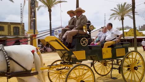 Spanisches-Paar-Fährt-In-Pferdekutsche-Mit-Zwei-Kutschern-Auf-Der-Messe-Von-Jerez,-Slowmo