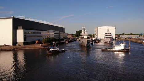 Aerial-View-Of-Tug-Boats-Tied-To-Forward-Bow-Of-Luxury-Yacht-Assisting-Docking-Procedure-At-Oceanco-Shipyard-Marina