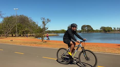 Bilder-Eines-Großen-Sees-Mitten-Im-Stadtpark-Von-Brasilia-Mit-Einem-Vorbeifahrenden-Radfahrer-An-Einem-Sommertag