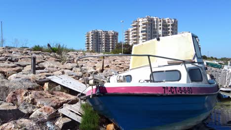 Ein-Altes-Motorboot,-Das-An-Einer-Felsigen-Küste-Festgebunden-Ist,-Steigt-Dann-Aus-Der-Luft-Auf,-Um-Im-Hintergrund-Apartments-Und-Eigentumswohnungen-Zu-Sehen