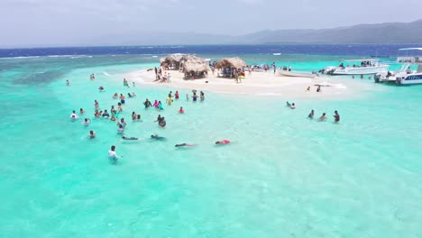 Aerial-orbit-shot-of-many-tourist-swimming-and-enjoying-crystal-clear-water-of-Caribbean-Sea---Paradise-Island,Dominican-Republic