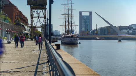 Menschen,-Die-Im-Hafen-Von-Madero-Spazieren-Gehen-Und-Fotografieren,-Mit-Der-Fregatte-Sarmiento-Und-Der-Brücke-Der-Frau-Im-Hintergrund-Bei-Tageszeitraffer