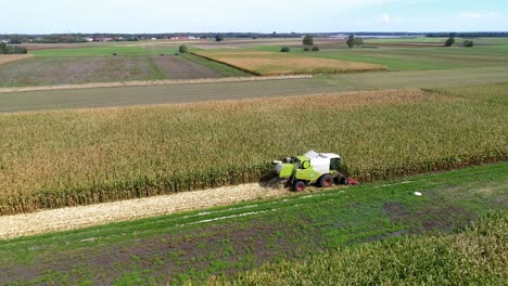 4K-Aerial-slow-motion-shot-of-corn-being-harvested-by-big-combine-harvester-at-noon-on-agricultural-fields-in-Bavaria,-Germany