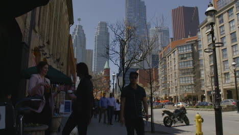 Pedestrians-walk-down-a-busy-sidewalk-in-downtown-Toronto,-Canada-on-a-warm,-spring-day