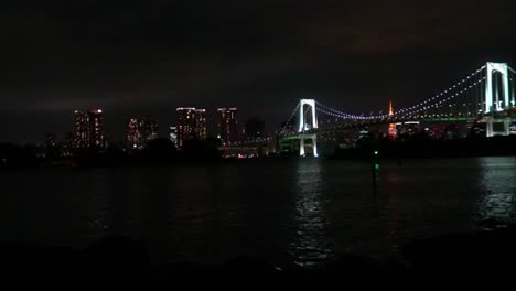Zeitraffer,-Der-Blick-Auf-Die-Regenbogenbrücke,-Den-Tokyo-Tower-Und-Die-Spiegelung-Des-Meeres-Bei-Nacht