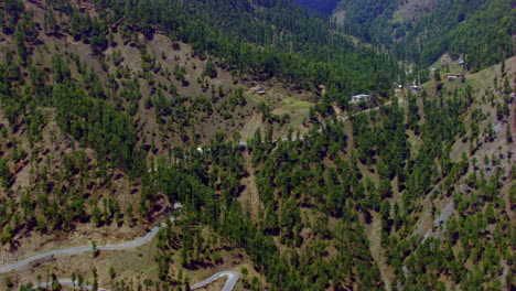 Aerial-smooth-drive-over-the-mountains-top-to-the-picturesque-valley,-showing-roads,-houses-and-forest-of-the-valley