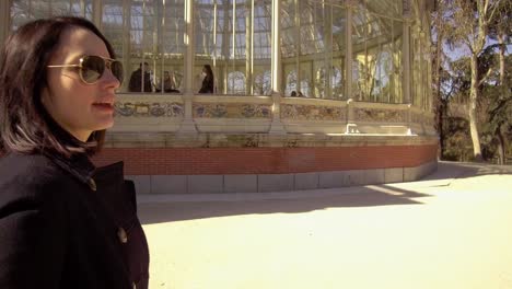 Female-tourist-walking-outside-Palacio-de-Cristal-in-Retiro-park,-Madrid