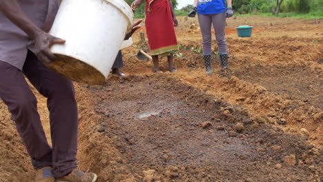 An-African-Man-Dumps-a-Bucket-of-Water-Onto-a-Dry-Garden-Bed-in-Rural-Zimbabwe,-Africa-in-Slow-Motion