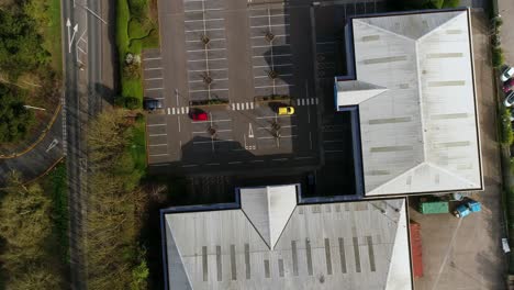 Antena-De-Arriba-Hacia-Abajo-De-Un-Aparcamiento-Casi-Vacío-En-Un-Pequeño-Parque-Comercial,-Con-Tres-Coches-De-Diferentes-Colores