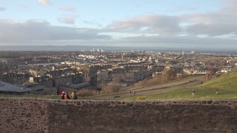 Toma-Panorámica-Desde-Calton-Hill-Con-Gente-Caminando-En-Primer-Plano-Con-Una-Bonita-Luz-De-Puesta-De-Sol-Y-Nubes-Con-Vistas-A-La-Ciudad-De-Edimburgo,-Escocia-Y-El-Océano-Atlántico-En-El-Fondo