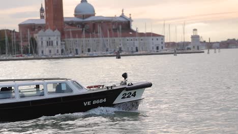 Slow-motion-shot-of-boats-sailing-past-famous-landmarks-in-Venice,-Italy-at-sunrise